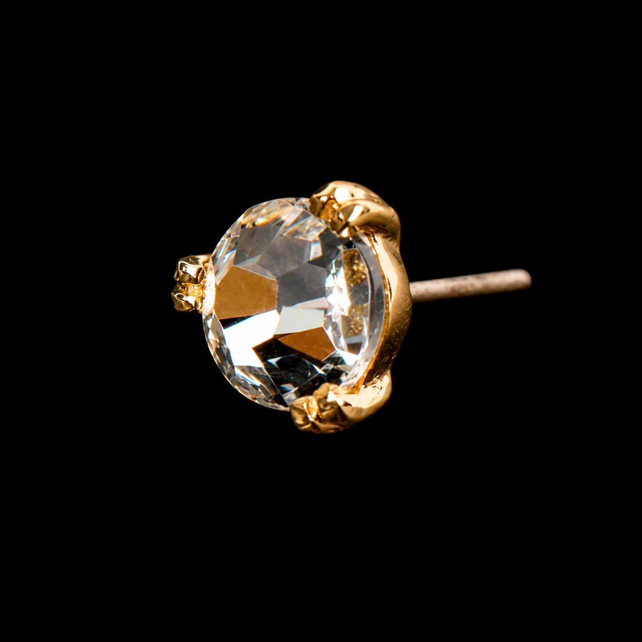 A clear cubic zirconia held in gold claws on a threadless post, photographed on black.