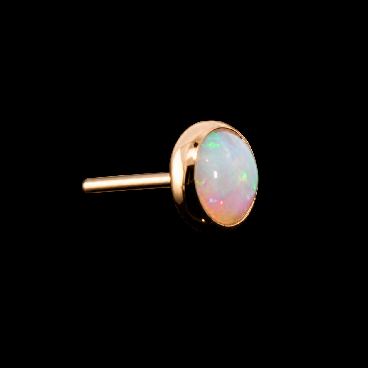 An opal cabochon in a polished gold bezel, its surface flashing green and pink, on black.