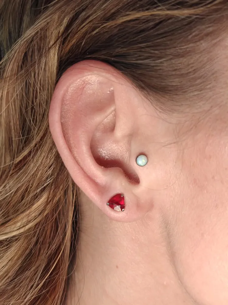 Curated ear — tragus piercing with opal end and a red-gem lobe